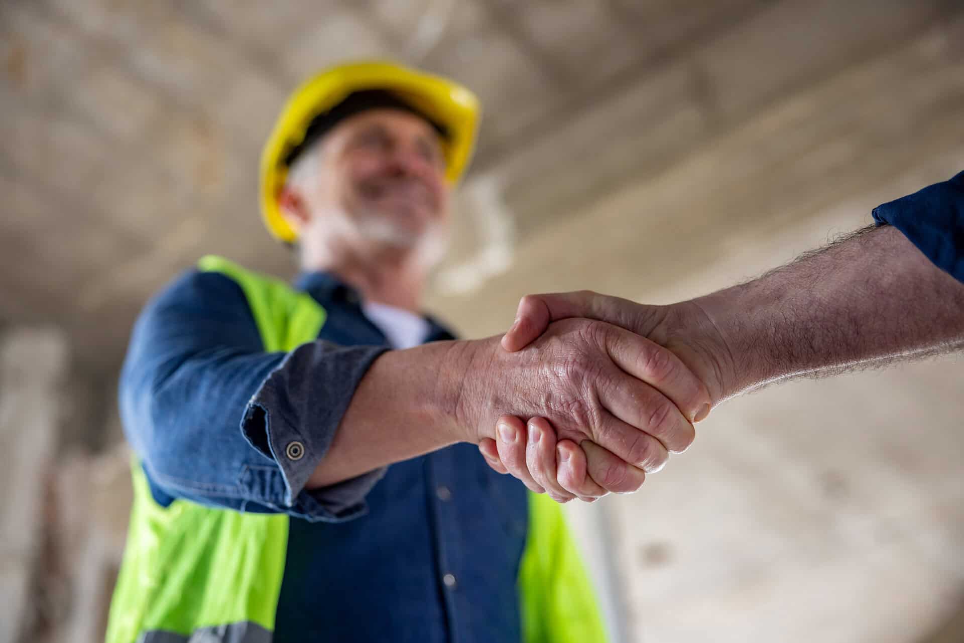 A commercial roofing consultant shakes hands with a client at a job site.