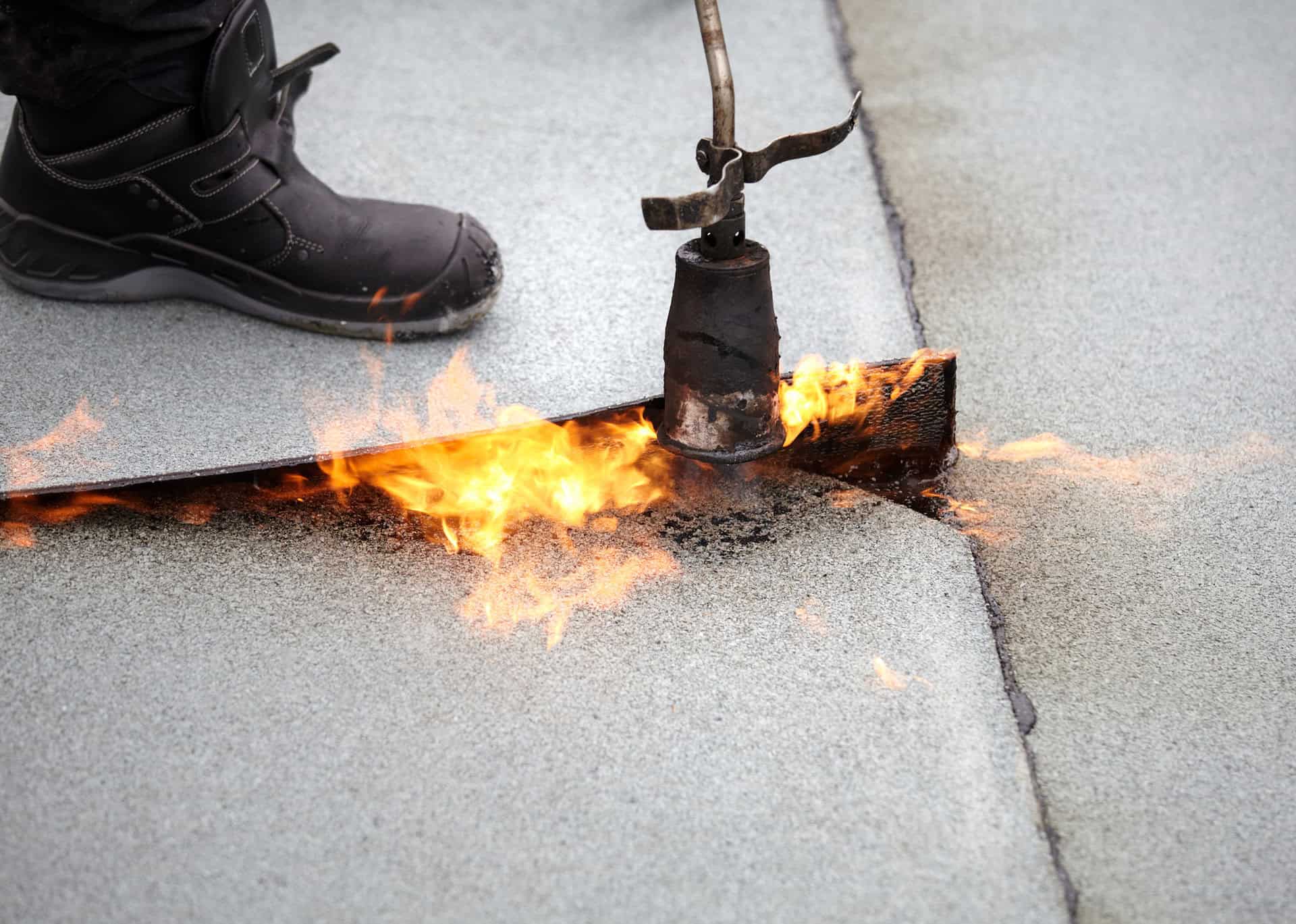 A roofing worker uses a torch to heat roofing tar to repair a commercial roof.