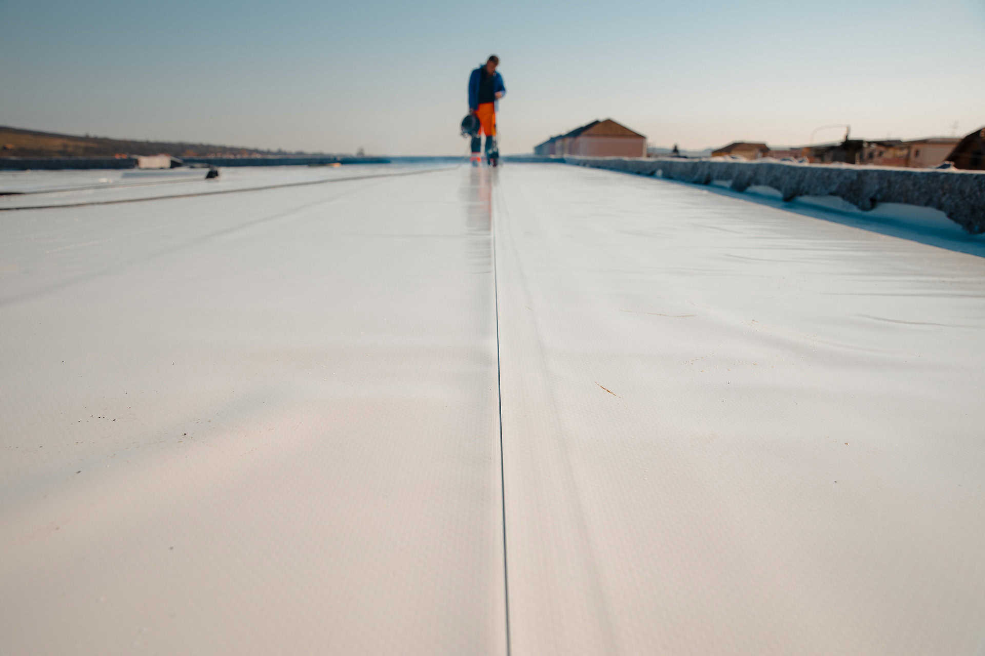 A worker stands on a white flat newly constructed roof.